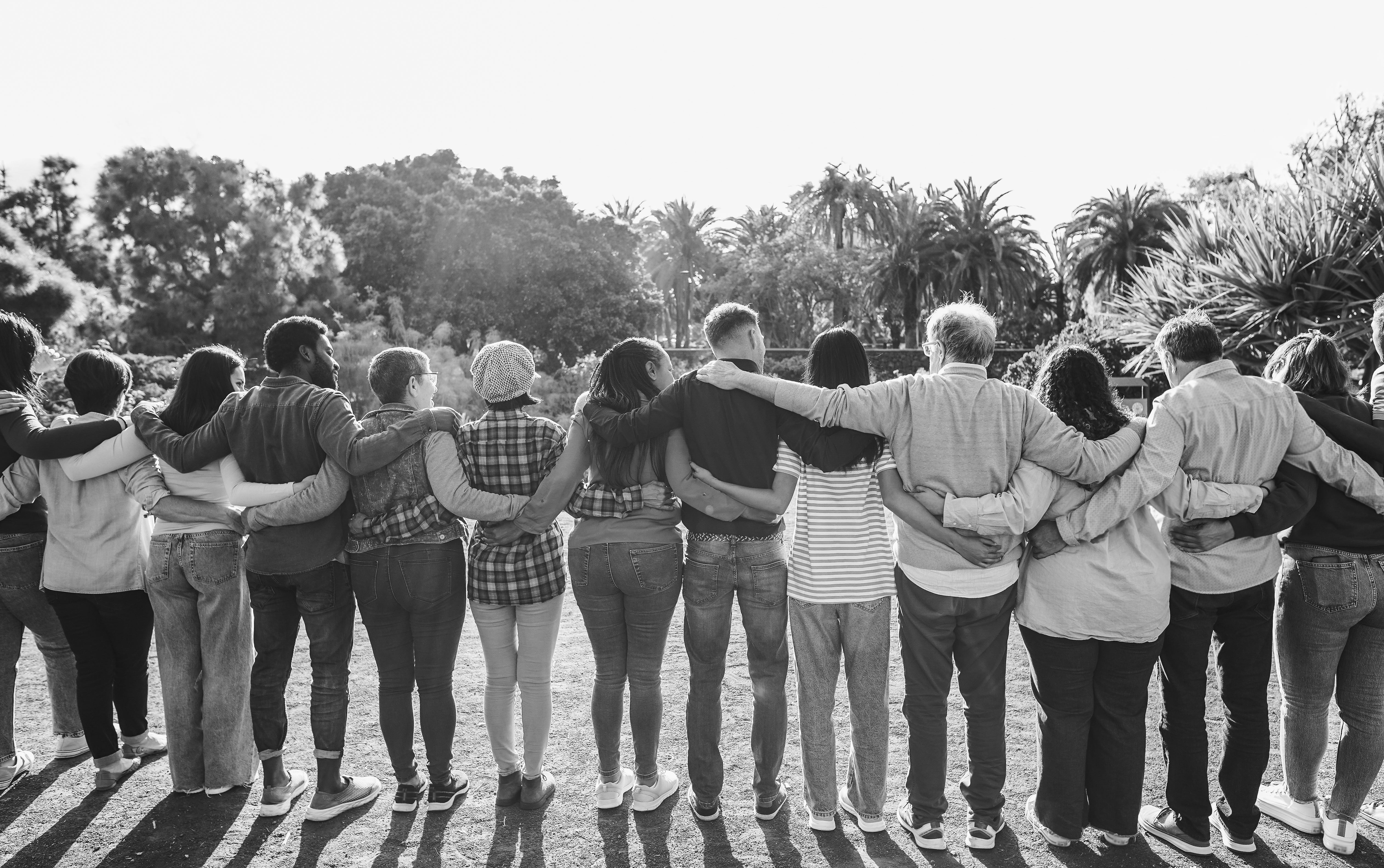 black and white photo of a group of people standing in a circle with arms around each other in a park.