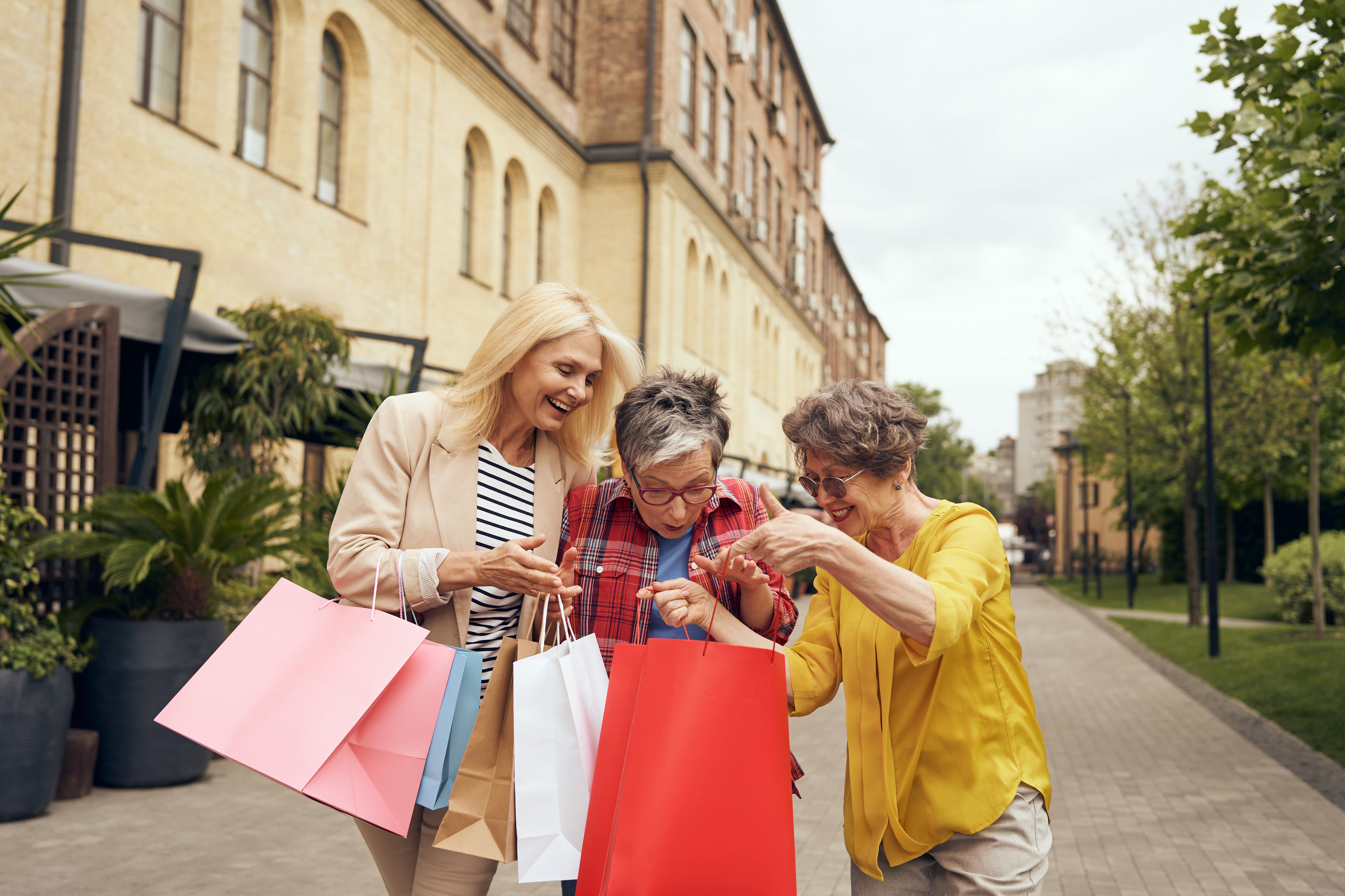Three older women looking at shopping bags excitedly on a city street